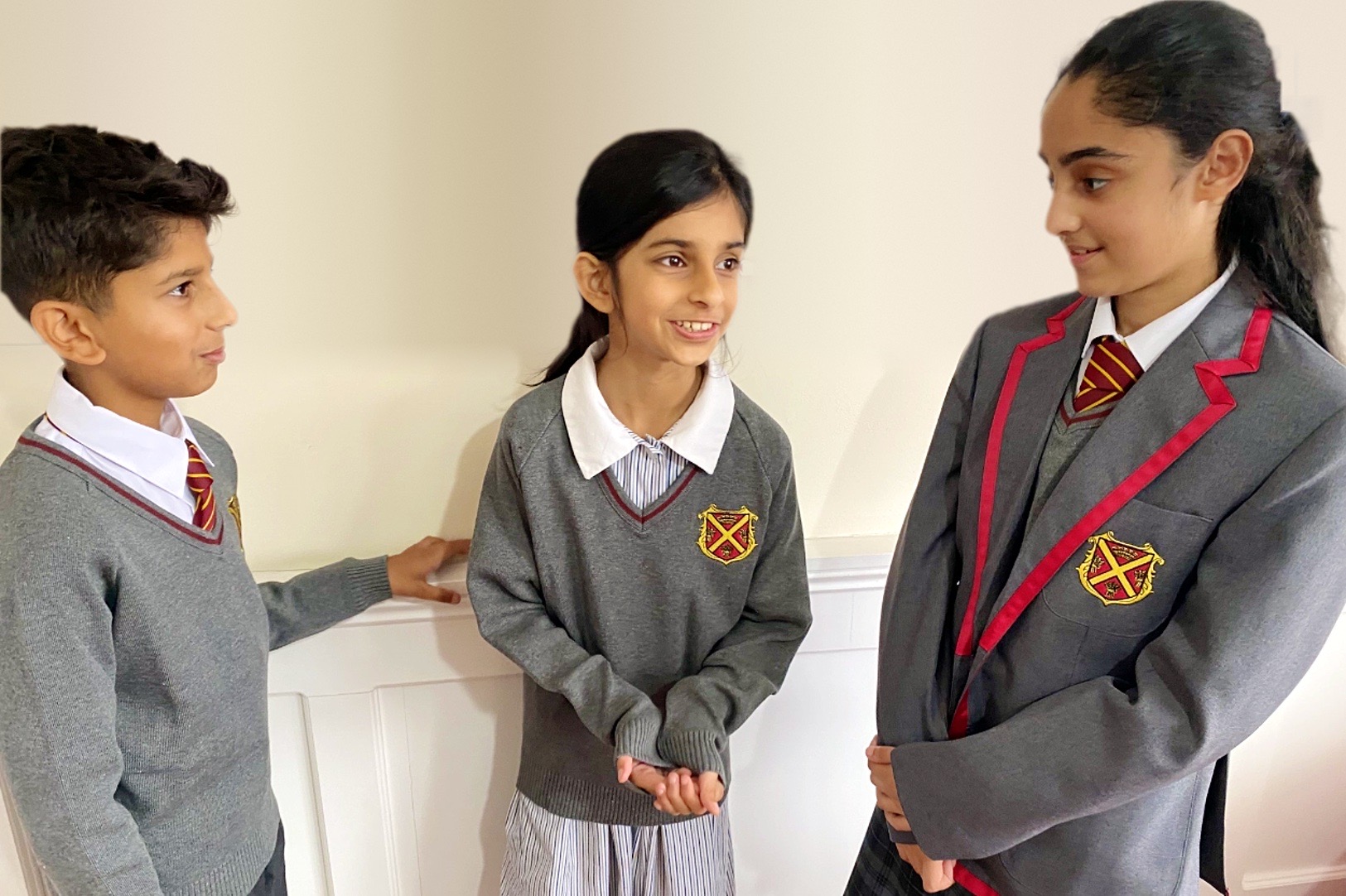 Three pupils in Queen's Square uniform, grey jumpers and blazers with the crest, talking together